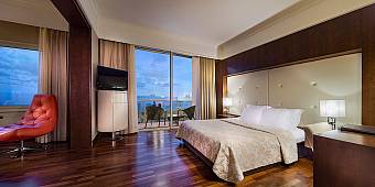 Hotel room with double bed, balcony, red lounge chair, and ocean view