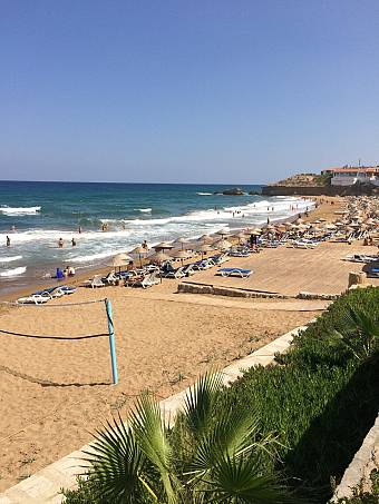 Sandy beach with lounge chairs, umbrellas, and volleyball net by the sea