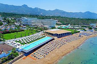 Aerial view of resort with pools, beach umbrellas, and mountains in background