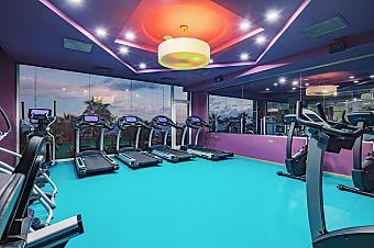 Fitness room with treadmills and cardio machines facing large mirrors and windows