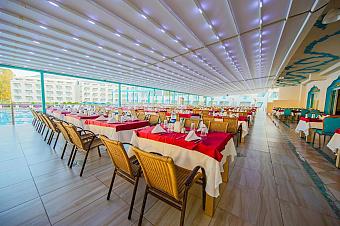 Covered restaurant terrace with long rows of tables and bright seating areas.