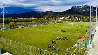 Outdoor football training fields with multiple pitches and teams practicing near mountains.