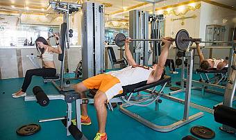 Gym workout area with athletes using weight machines and free weights.