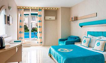 Bright hotel room with double bed, sofa seating, desk, and balcony door.
