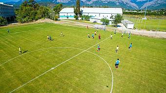 Football team training session on a grass pitch with mountain scenery behind the facility.