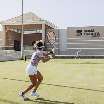 Female athlete playing tennis on grass court near Soma Sports Arena