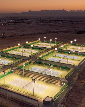 Wide view of multiple lit tennis courts at dusk in sports complex