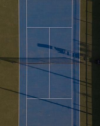 Overhead view of single blue tennis court with shadows cast