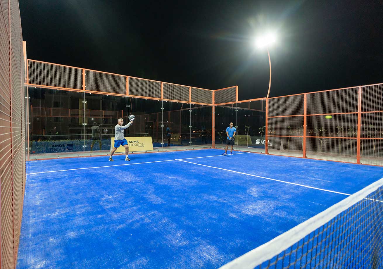 Zwei Athleten spielen Padel-Tennis auf einem blau beleuchteten Platz bei Nacht