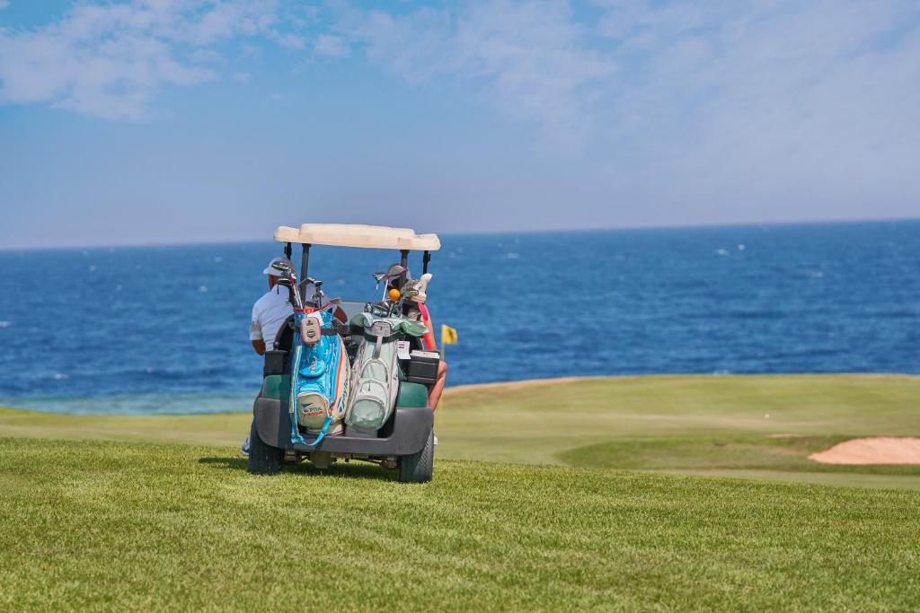 Golfcart mit zwei Golftaschen auf einem Fairway am Meer, im Hintergrund blauer Ozean und bewölkter Himmel