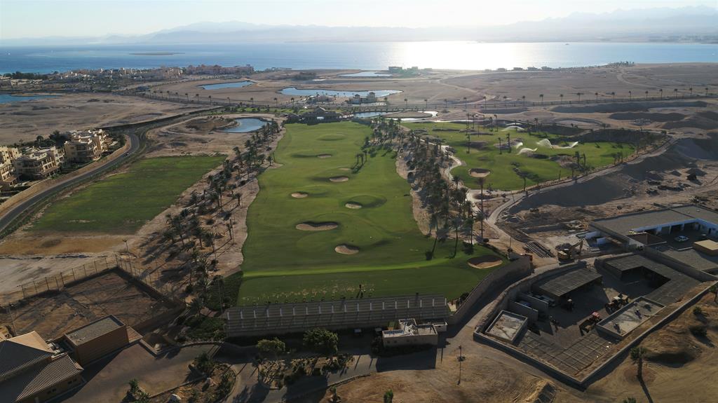 Luftaufnahme einer Wüstengolfanlage mit palmenbestandenen Fairways, Bunkern und Wasserlagunen nahe dem Meer