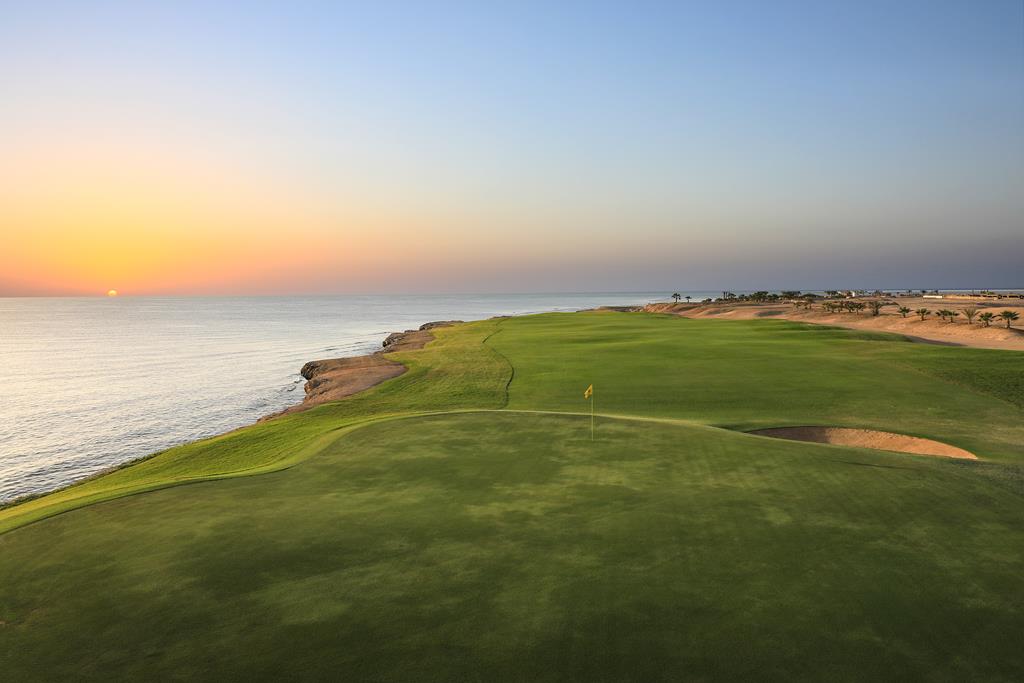 Küstengrün bei Sonnenaufgang mit Fahne, Sandbunker und Horizont über dem Meer