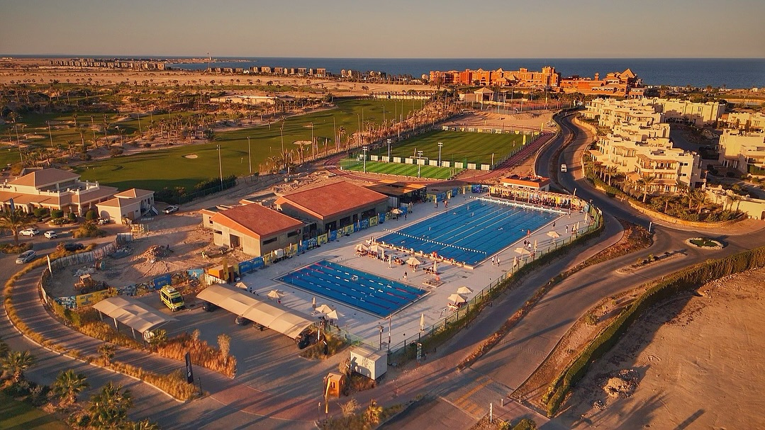 Luftaufnahme eines Freibad-Langbeckens neben Golfplatz und Resortgebäuden bei Sonnenuntergang, Trainingscamp-Anlage