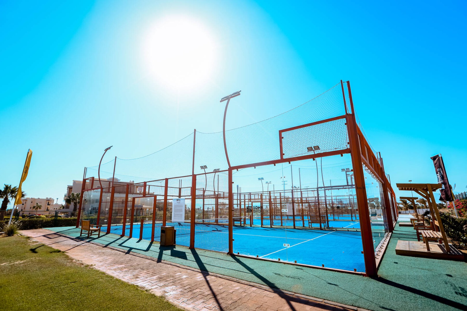 Outdoor-Padelplätze mit blauem Belag und Glaswänden unter greller Sonne an einem Trainingscamp-Standort