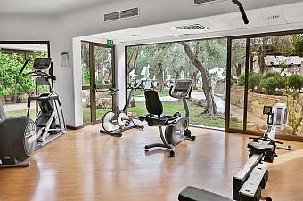 Fitnessraum mit Cardio-Geräten und Krafttrainingsausrüstung mit Blick auf den Gartenbereich