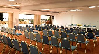 Präsentationssaal mit Reihen blauer Stühle und einem vorderen Tisch für Teamseminare oder Workshops