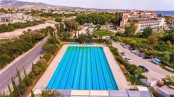 Luftaufnahme eines Langbahn-Schwimmbeckens mit Parkplatz und Landschaft im Hintergrund