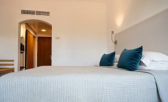 Hotelzimmer mit großem Bett, grauer Bettwäsche und türkisfarbenen Kissen in minimalistischem Design