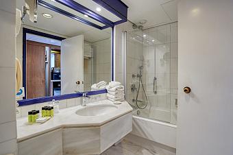 Badezimmer mit weißen Fliesen, Badewanne und Ablage mit Pflegeprodukten und gefalteten Handtüchern