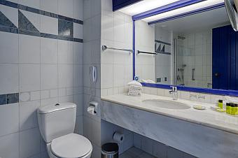 Weiß gefliestes Badezimmer mit Spiegel, Waschbecken und modernen Armaturen, vorbereitet für Gäste