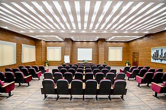 Conference hall with rows of red chairs facing a projection screen