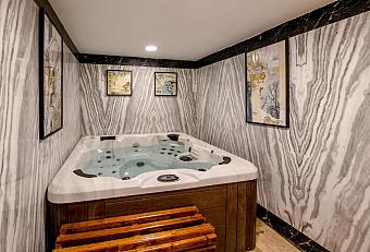 Jacuzzi hot tub in a spa room with patterned gray marble walls, wooden bench, and framed wall art