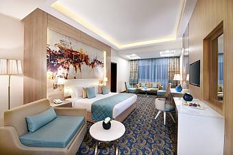 Modern hotel room with double bed, sofa, blue accents, and patterned carpet