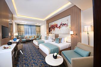Spacious twin room with two beds, blue decor, seating area, and large window