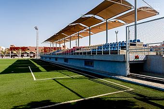 Überdachter Sitzbereich mit blauen Stühlen entlang des Spielfeldrands