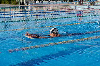 Swimmer in cap training with kickboard in outdoor Olympic-size pool