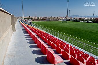 Reihe roter Kunststoffsitze mit Blick auf das Trainingsfeld des Fußballcamps