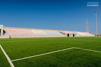 Eckansicht des Fußballfelds mit pastellfarbenen Tribünen unter klarem Himmel