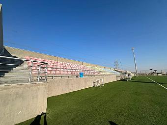 Betontribünen mit pastellfarbenen Sitzen neben dem Trainingsfeld des Fußballcamps