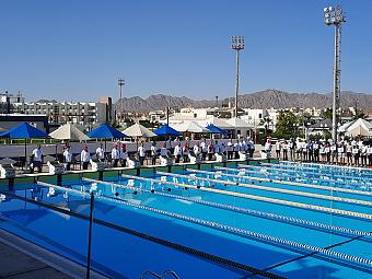 Olympic pool setup with swimmers and coaches during a training camp practice under clear skies