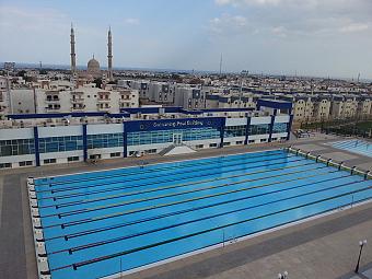 Aerial view of 50m Olympic swimming pool building within city area, suitable for swim training camps
