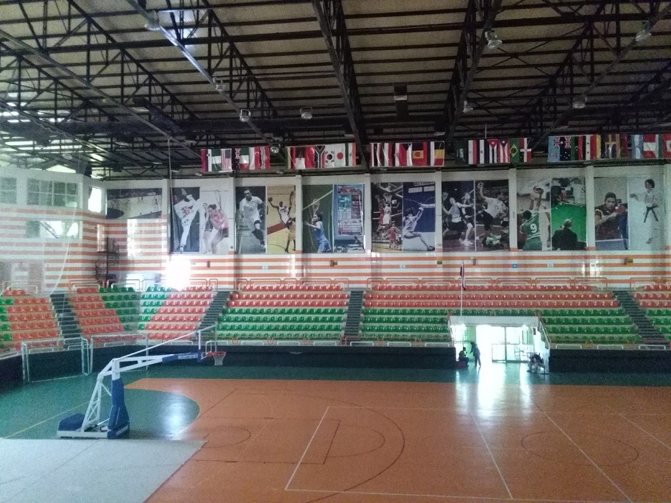 Panorama einer Indoor-Sporthalle mit Spielfeld, Basketballkorb, Zuschauertribünen und Flaggen unter dem Dach.
