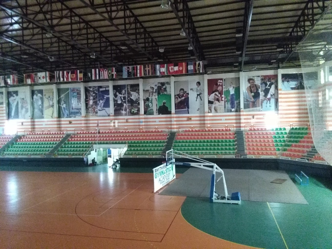 Weitwinkelblick in eine Indoor-Arena mit Spielfeldlinien, Basketballkorb, Tribünen und Sportbannern.