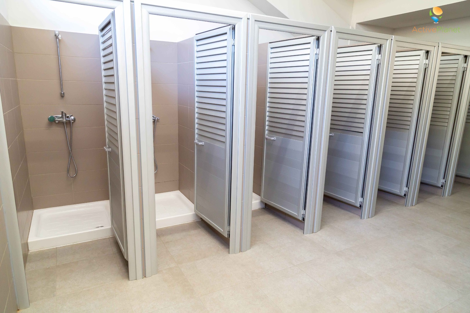 Row of clean shower stalls with tiled walls and individual doors in sports facility