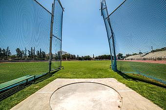 Hammerwurf-Trainingsbereich mit Sicherheitsnetzen und Rasenfläche unter klarem blauem Himmel
