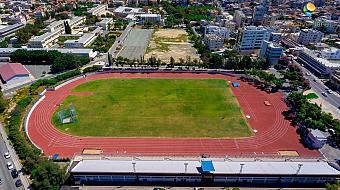 Luftaufnahme einer roten Laufbahn und eines grünen Spielfelds, umgeben von Stadtgebäuden, genutzt für Trainingslager und Übungseinheiten
