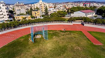 Luftaufnahme einer roten Laufbahn und eines grünen Spielfelds, umgeben von Stadtgebäuden