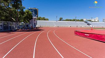 Kurve der Laufbahn mit Trainingsgeräten und schattigen Zuschauertribünen