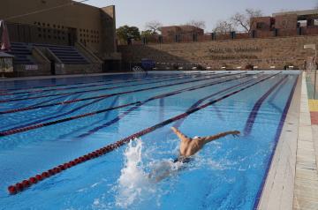 Outdoor lap pool with lane ropes, showing a swimmer entering the water during training.