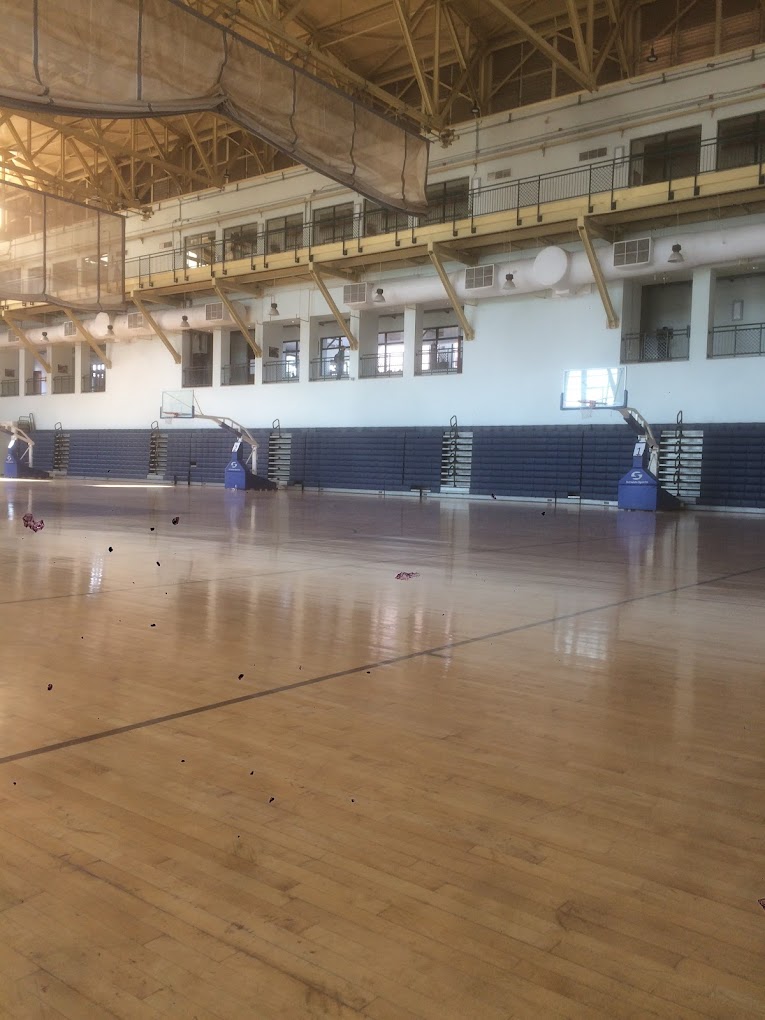 Spacious indoor sports hall with an empty wooden court, basketball hoops, and folded bleachers.