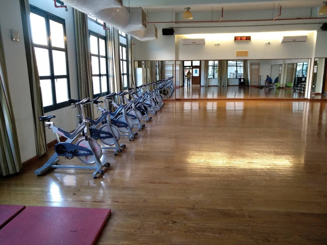 Indoor fitness studio with a row of stationary spin bikes, wooden floors, and a mirrored wall.