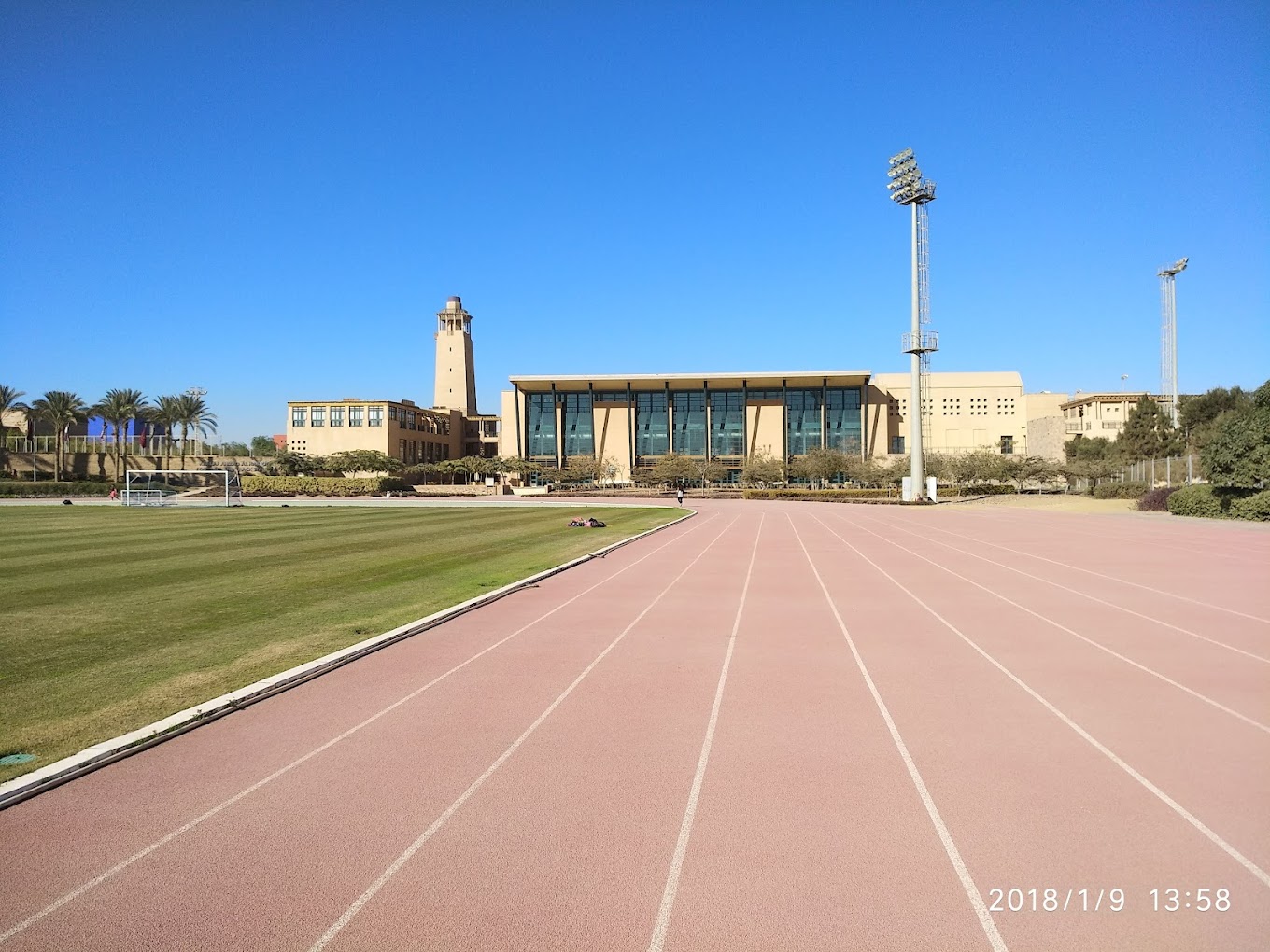 Running track lanes next to a grass field and floodlights, with a timestamp overlay.