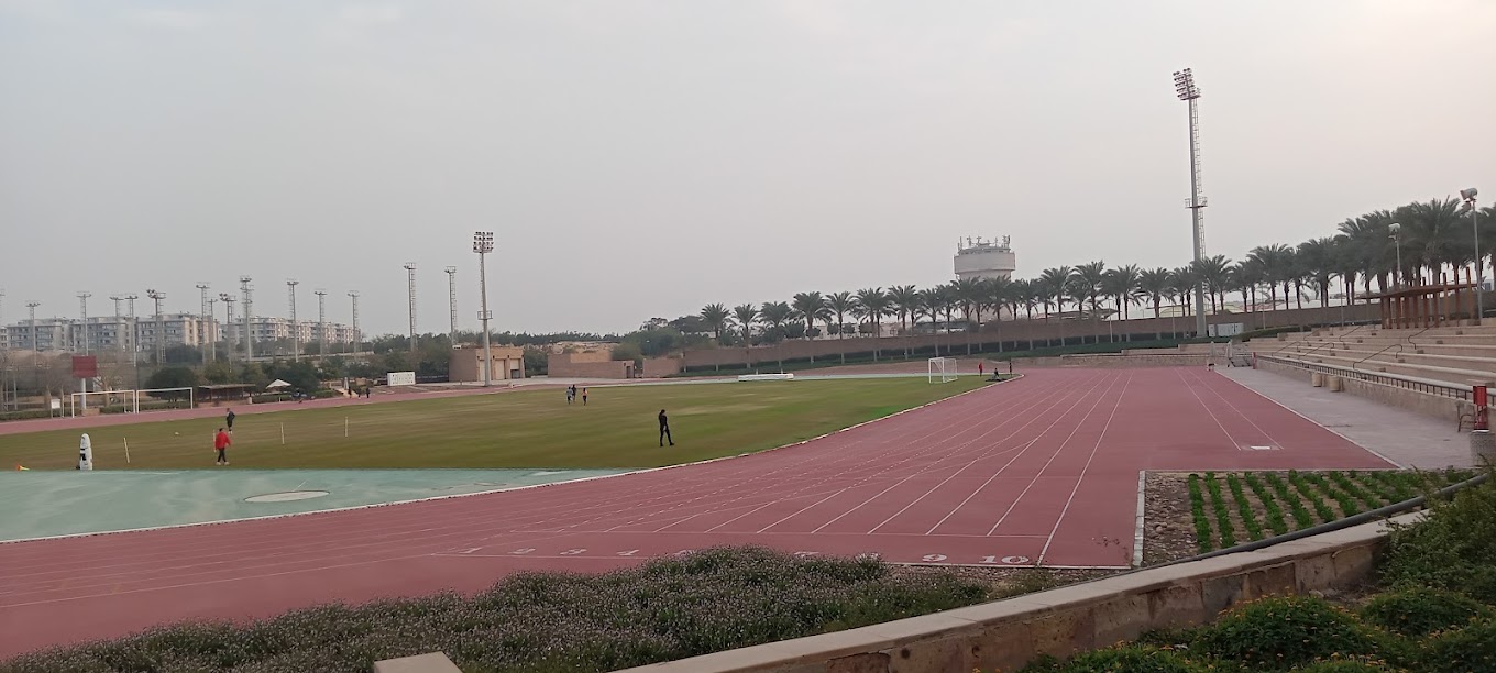 Athletics track beside stadium seating and floodlights, with a grass field in the center.