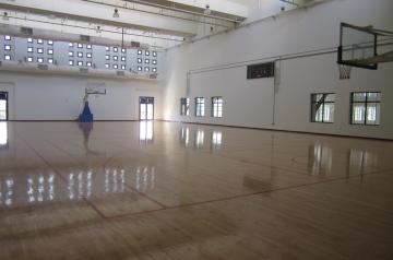 Empty indoor gym with a polished wooden court and a basketball hoop.