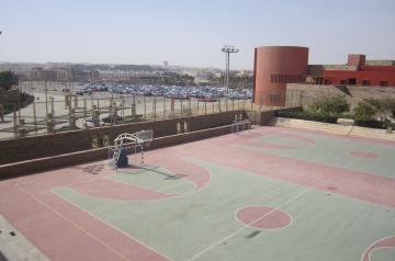 Empty outdoor multi-sport court with basketball hoops, overlooking nearby campus buildings and parking areas.