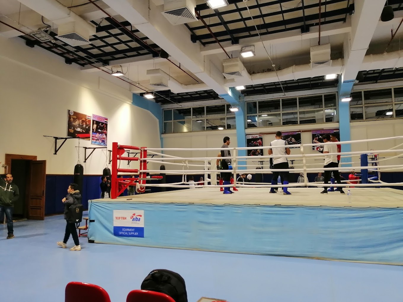 Indoor-Boxhalle mit einem Boxring und Athleten, die in der Nähe trainieren.